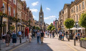 Pedestrianised town centre street with shoppers and a church spire in the distance